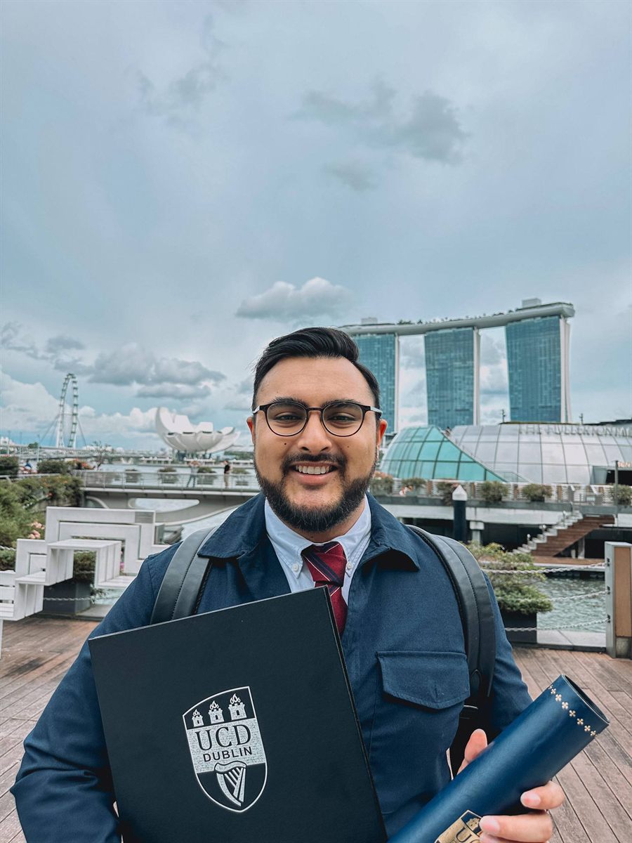 Afiq Syahiran on the Marina Bay waterfront in Singapore, holding a University College Dublin degree folder.